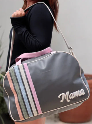 Woman carrying a gray Mama duffle bag with pastel stripes, styled with a pink graphic tank and pink bow skort.