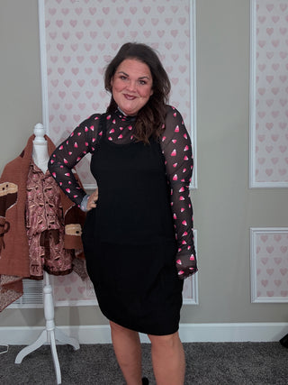 Woman wearing a black dress with pink candy corn patterns in a room with patterned wallpaper.