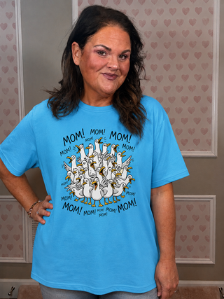 Woman wearing a blue t-shirt with a graphic design and text, standing in a room with heart-patterned wallpaper.