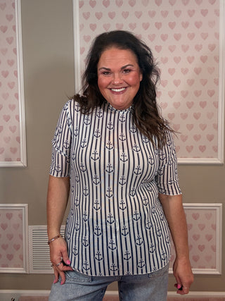 Woman wearing a nautical mesh top with blue anchors standing in a room with heart-shaped wallpaper.