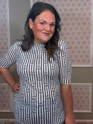 Woman wearing a nautical mesh top with blue anchor pattern against a heart-patterned wall.