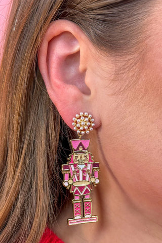 Close-up of a person wearing a pink and gold nutcracker earring.