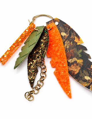 A feather-themed earrings featuring three stylized feathers: one green glitter feather, one orange glitter feather, and one camouflage-patterned feather, attached to a gold-tone split ring and chain.