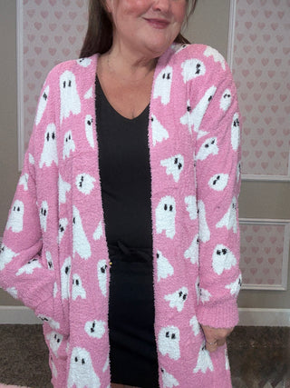Person wearing a pink cardigan with ghost patterns against a heart-patterned wall.