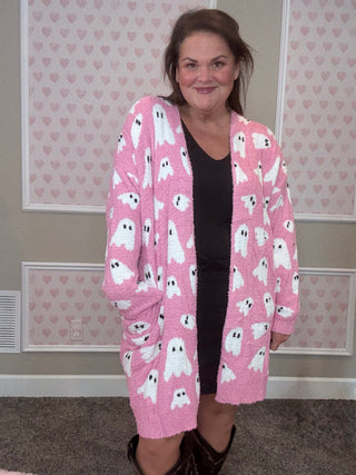 Woman wearing a pink cardigan with ghost pattern in a room with heart-patterned wallpaper.