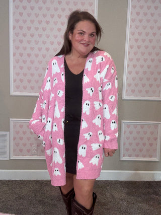 Person wearing a pink cardigan with ghost patterns in a room with heart-patterned wallpaper.