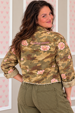 Blakeley Hunting Season women's camo jacket featuring floral camouflage print, embroidered Hunting Season lettering on back, sequin duck chest patch, button-front closure, utility sleeve pockets, and raw hem, available in sizes S/M–3X.
