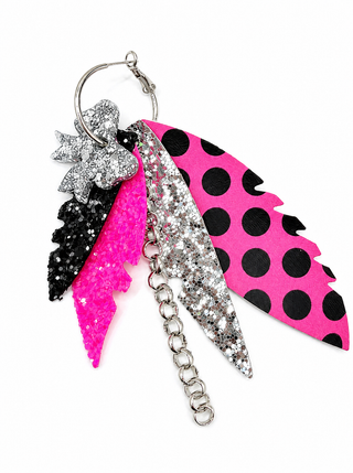 A colorful feather earrings  featuring three feathers: one bright pink glitter feather, one black glitter feather, and one silver glitter feather with black polka dots, attached to a silver metal ring and chain.