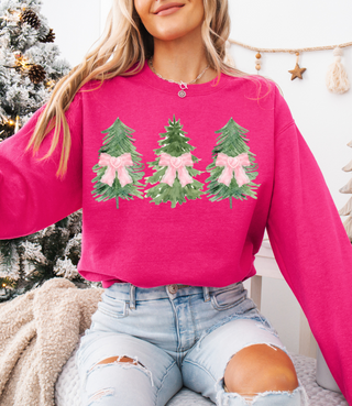 Person wearing a pink sweatshirt with Christmas tree designs in front of a decorated Christmas tree.