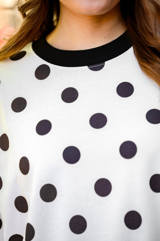 Close-up of a white shirt with black polka dots worn by a person.