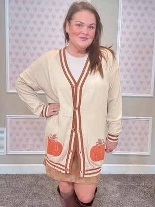 Woman wearing a beige cardigan with orange pumpkin designs in a room with heart-patterned wallpaper.