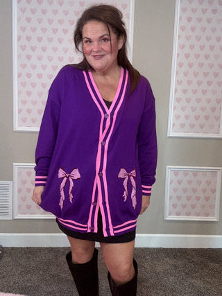 Person wearing a purple cardigan with pink accents in a room with patterned wallpaper.