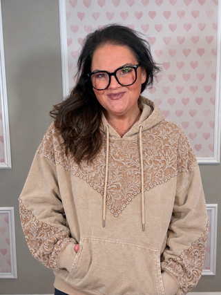 Sterling Kreek Tooled Frontier Hoodie in tan featuring intricate floral western tooled-inspired lace detailing across chest, shoulders and sleeves, drawstring hood, kangaroo pocket, and ribbed cuffs.