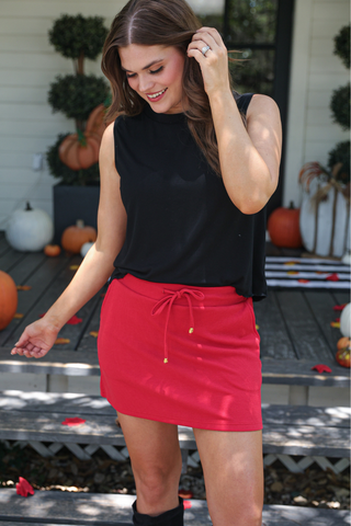 Woman wearing a black top and red skirt standing outdoors with pumpkins in the background