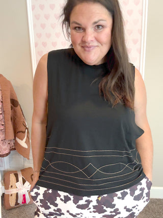 Woman wearing a black sleeveless top and patterned pants indoors.