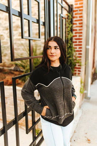 Woman wearing a black and gray sweater with white trim standing in front of a metal gate.