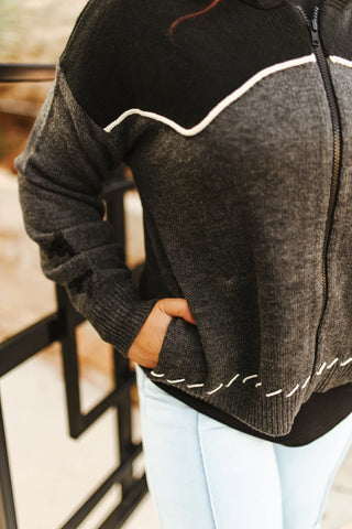 Person wearing a black and gray sweater with white stitching in an indoor setting