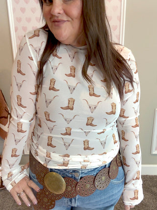 Person wearing a sheer top with cowboy boot pattern and jeans.