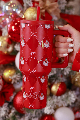 Red mug with white patterns held in front of a decorated Christmas tree.