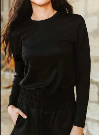 Person wearing a black long-sleeve top against a stone wall background