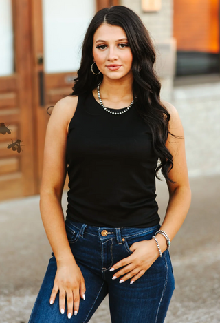 Woman wearing a black tank top and blue jeans outdoors.
