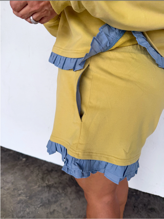 Yellow ruffle lounge set with cropped sweatshirt and matching shorts in a soft pastel yellow with blue trim details.