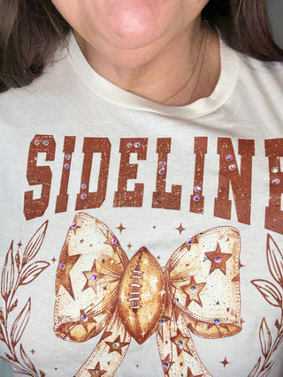 White shirt with 'SIDELINE' text and decorative bow design.