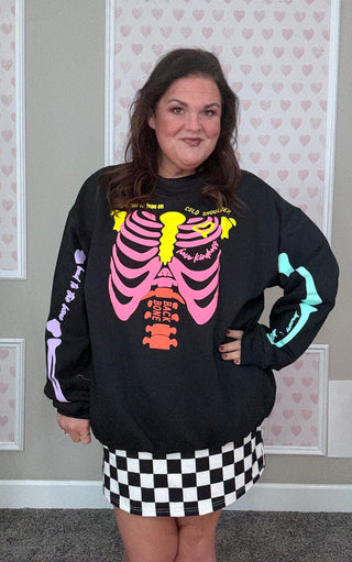 Person wearing a black sweatshirt with colorful skeleton design in front of a heart-patterned wall.