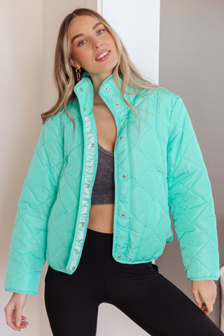 Woman wearing a turquoise puffer jacket with a neutral background