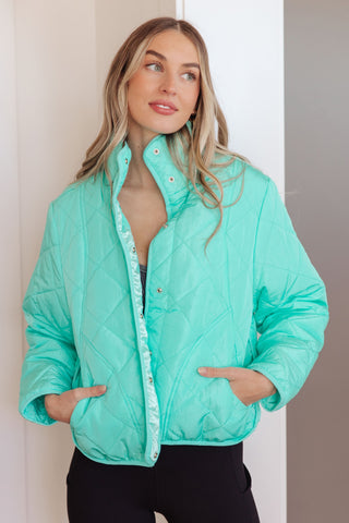 Woman wearing a turquoise quilted jacket against a neutral background
