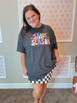 Person wearing a dark gray t-shirt with colorful text in a room with heart-patterned wallpaper.