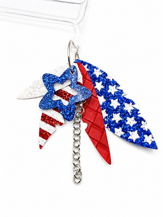 Patriotic-themed earrings featuring red, white, and blue glitter elements, including a star, stripes, and stars-and-stripes shapes, attached to a silver split ring and chain.