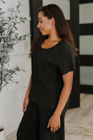 Woman wearing a black outfit standing indoors with a plant in the background