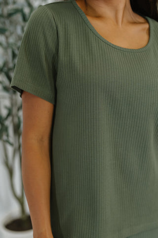 Person wearing a green ribbed t-shirt with a blurred background