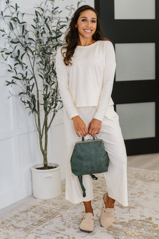 Woman in a white outfit holding a green handbag indoors.