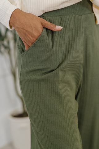Person wearing green ribbed pants with a blurred indoor background