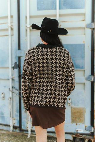 Person wearing a patterned jacket and black hat standing in front of a metal container.