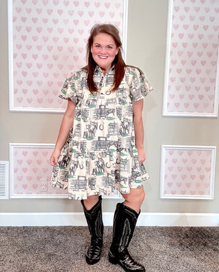 Woman wearing a western patterned dress and black boots standing in front of framed pictures with heart design.