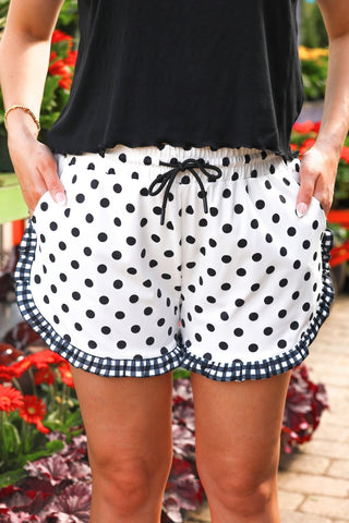 Person wearing black and white polka dot shorts with a blurred floral background