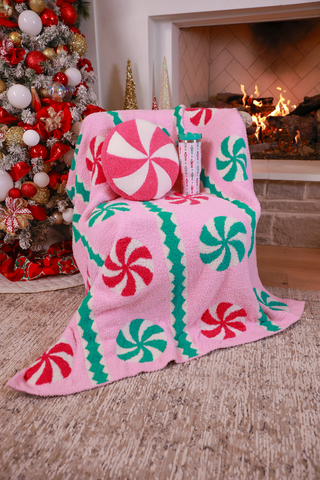 Pink candy cane patterned blanket draped over a chair in a cozy living room with a Christmas tree and fireplace.