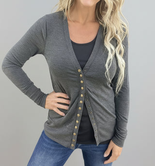 Woman wearing a gray cardigan with button details against a metallic wall.