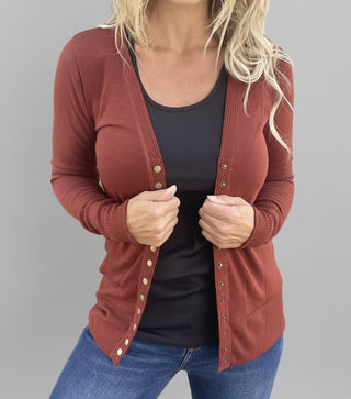 Woman wearing a rust cardigan over a black top and blue jeans against a corrugated metal background