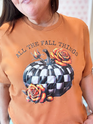 Person wearing an orange fall t-shirt with a black and white checkered pumpkin and roses design, text 'All the Fall Things'.
