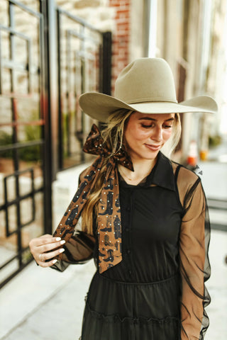 Woman wearing a beige hat and black dress with a patterned scarf outdoors.