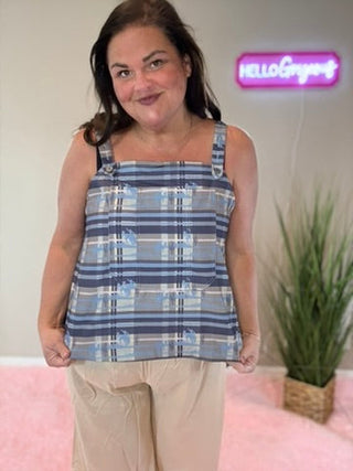Woman wearing a blue plaid top with beige pants in a room with a pink couch and plant.