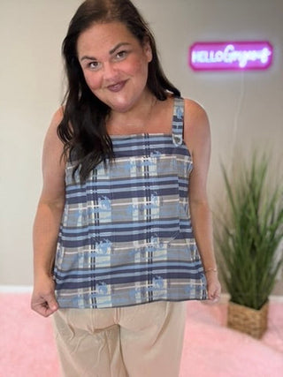 Woman wearing a blue plaid top and beige pants in a room with a plant and pink rug.