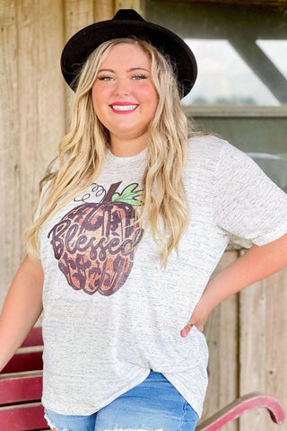 Woman wearing a white t-shirt with a graphic design and a black hat, standing outdoors.