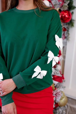 Woman wearing a green Christmas pullover with satin bows on sleeves, cozy festive outfit.