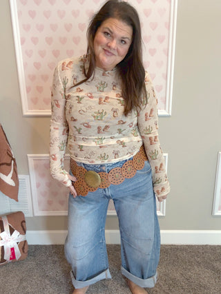 Model wearing the Cactus & Boots Mesh Top featuring a sheer long sleeve design with western print details, styled with jeans for a chic layered look.