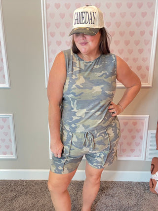 Person wearing a camouflage romper and 'GAMEDAY' cap indoors.